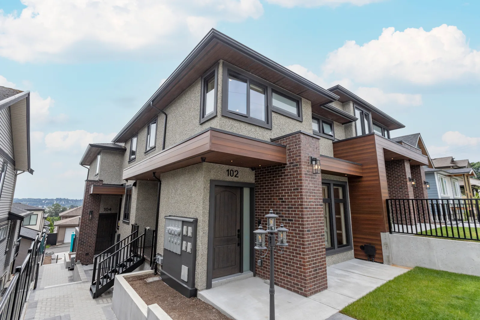 Two of the four front doors at the Majack Developments fourplex on Delestre Avenue in Maillardville, Coquitlam: the door of home 102 beside a shared bank of mailboxes, with the door of home 104 further along the side path