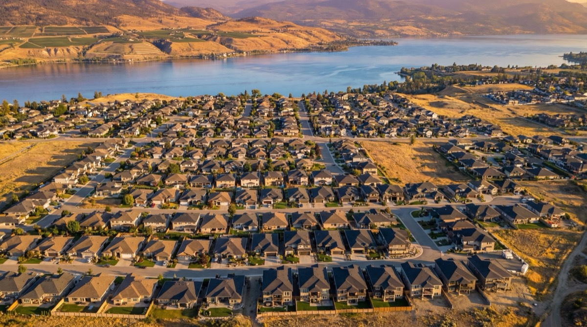 Aerial view of Kelowna residential neighbourhoods with Okanagan Lake in the background, showing single-family homes on MF1-zoned lots awaiting multiplex redevelopment