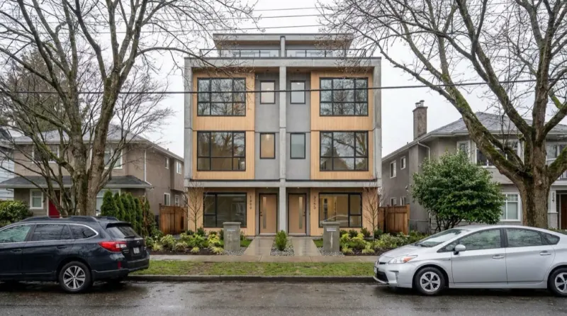 A finished side-by-side multiplex with wood and concrete panels between two older houses on a wet Vancouver street, illustrating the September 2026 gap between land cost and unit exit price